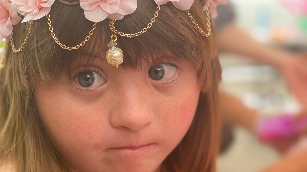 image of a girl with down syndrome a crown of flowers looking intently at the camera - best down syndrome awareness videos
